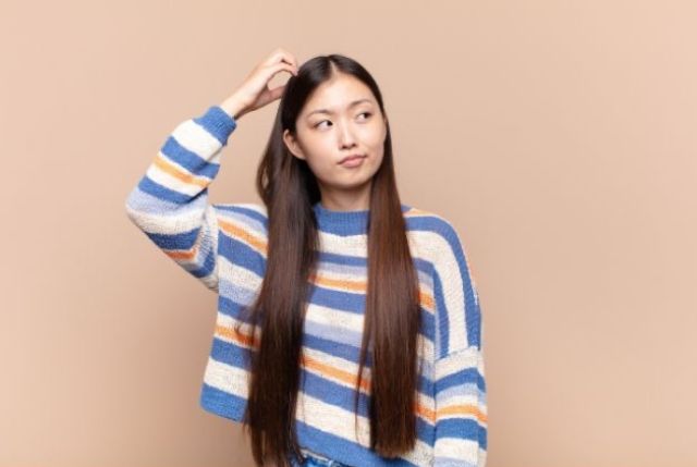 頭をかくロングヘアの女性