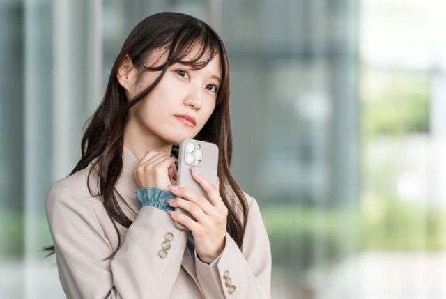 スマホを持って首を傾げるロングヘアの女性