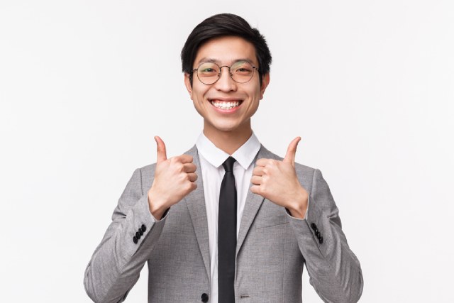 両手でサムズアップするグレーのスーツの男性