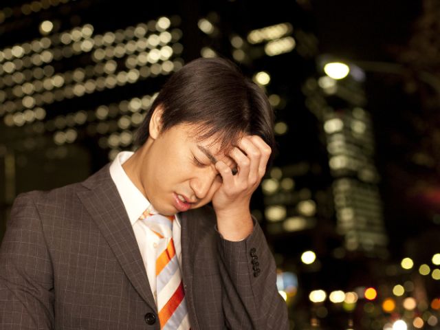 夜の街中で頭を抱えるスーツの男性
