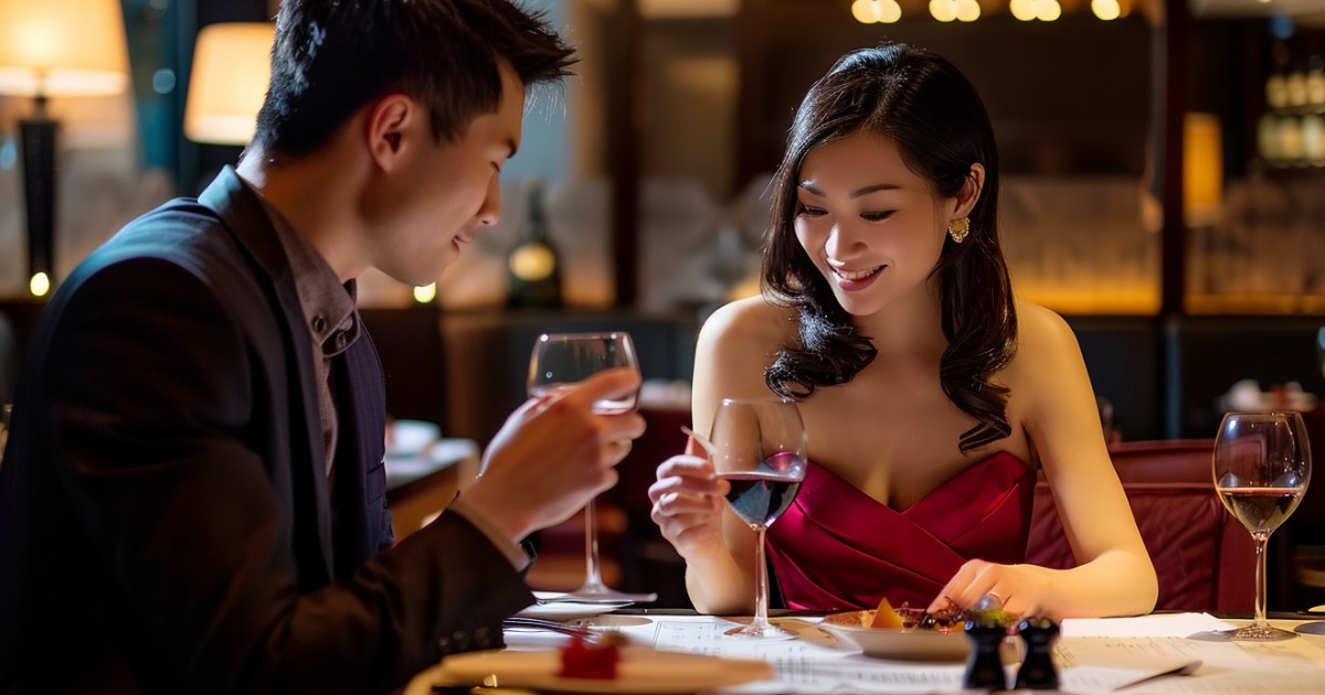 高級レストランのテーブルに座りワインを飲みながらメニューを見て微笑む日本人の男女