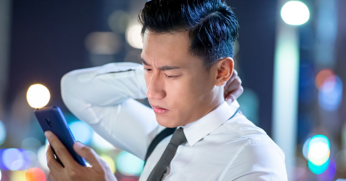 スマホを見ながら頭を抱えるスーツの男性