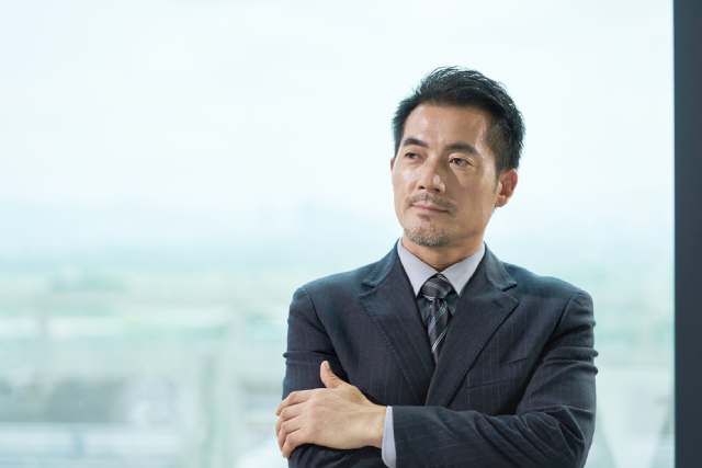 窓際で腕を組みながら考えた表情の男性