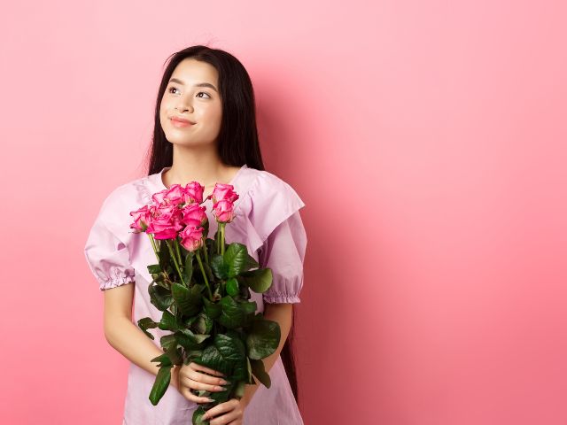 ピンクの壁の前に花束を持って立つ若い女性
