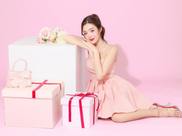 ピンク色の部屋でプレゼントの箱に寄りかかるピンク色のドレスを着た若い女性
