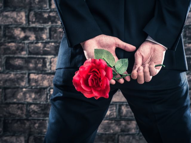 後ろ手に薔薇を一輪持つスーツの男性