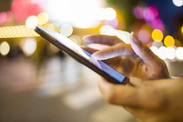 夜の街でスマホをいじる女性の手元