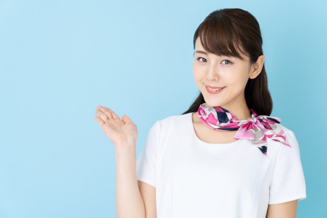 水色の背景の前にたつ白い服にスカーフを首につけた美容部員