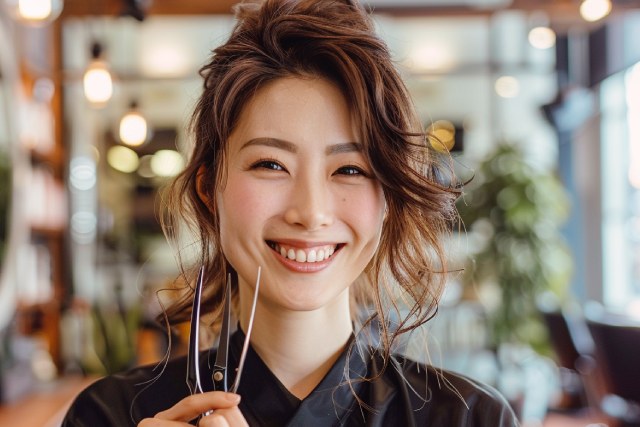 仕事道具のはさみを持って笑顔を見せる女性美容師