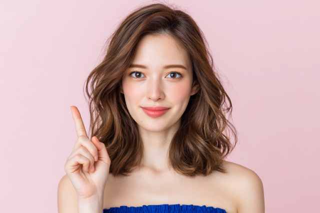 ピンクの背景の前で指を 本あげている女性