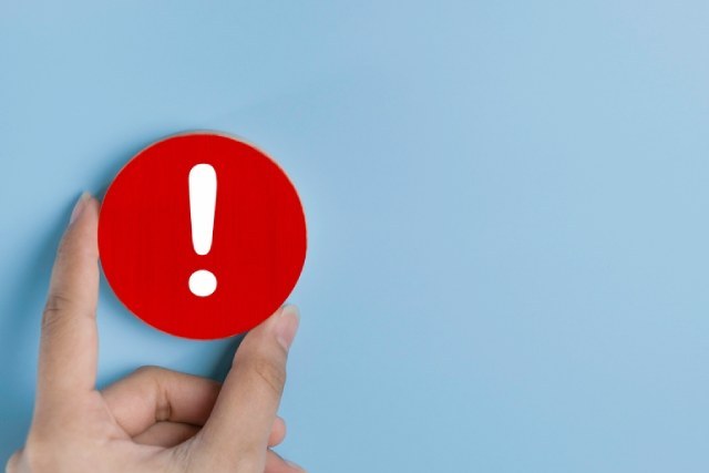 水色の背景と注意を促すエクスクラメーションマークと男性の手