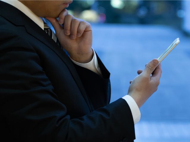 スマートフォンを片手に悩んでいる様子の男性