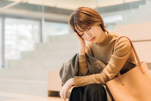 オフィスの階段に座って頭を抱える悩んでいる様子の女性