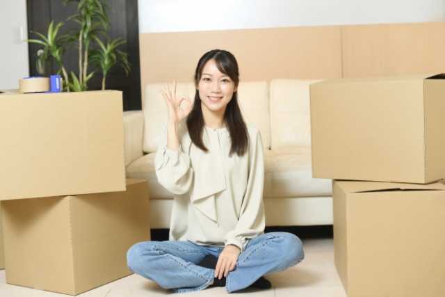 段ボールが山積みの部屋でOKサインを出して座っている女性