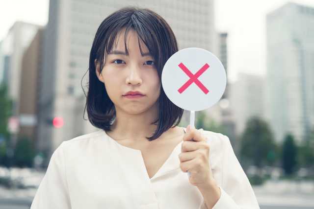 バツマークのプラカードをもつ若い女性