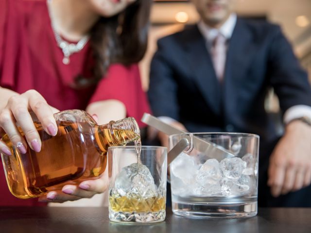 お酒を作っている赤いドレス姿の女性と隣に座るスーツ姿の男性