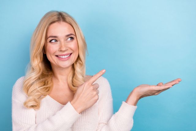 水色の背景の前で横を指さす女性