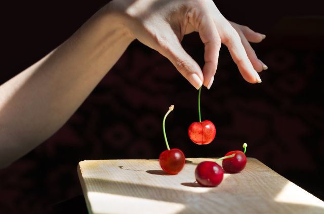 4つのさくらんぼのうち1つを持ち上げる女性の手