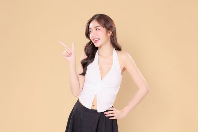 横を指さすワンピースの女性