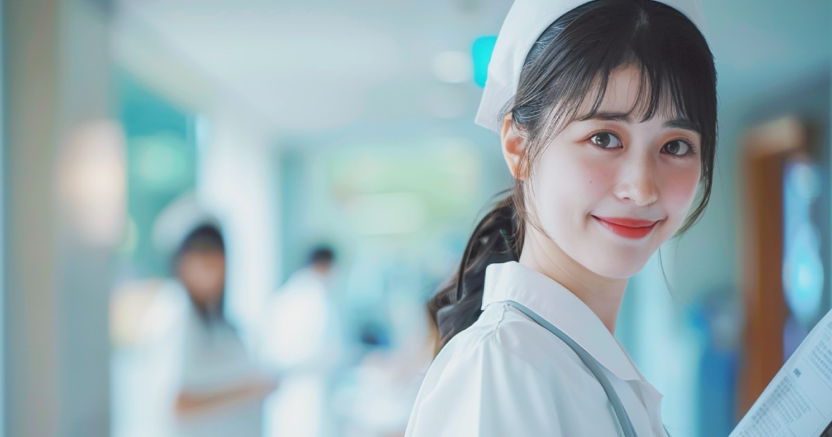 病院を背景に白い制服を着て笑顔でカルテを持つ日本人の若い女性看護師