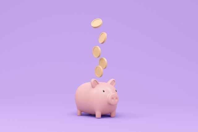 紫の背景の前にある豚の貯金箱と浮いているお金