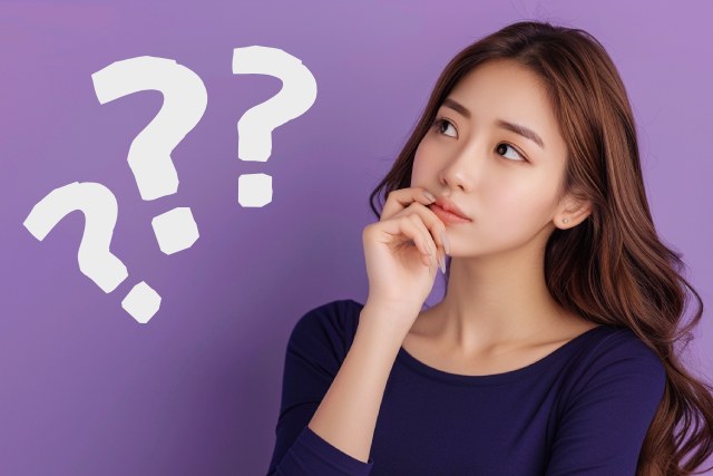 紫色の背景にネイビー色のワンピースを着て考える様子の茶髪の日本人女性