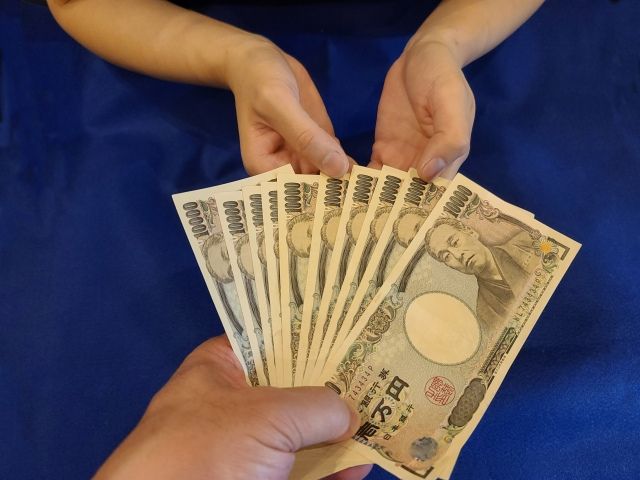男性が女性に一万円札をたくさん手渡ししている