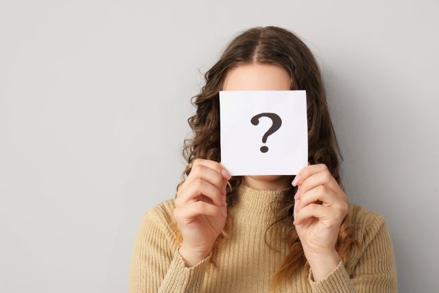 ハテナマークの紙を顔の前で持つ女性