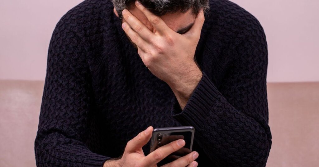 携帯を持って頭を抑える男性