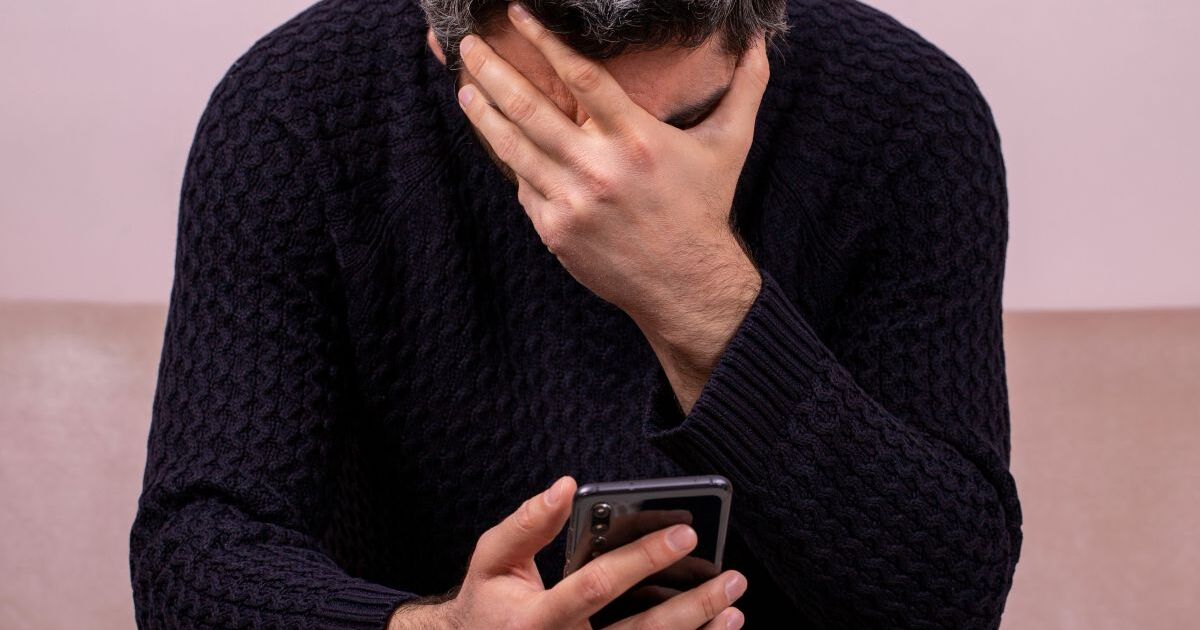 携帯を持って頭を抑える男性