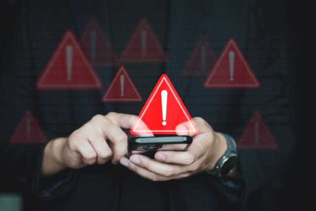 スマホを持つ手に表示されている赤い注意を促すマーク