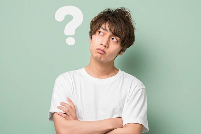 白いTシャツを着た茶髪の若い男性が腕を組んで考えている様子