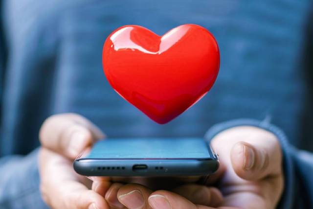 青い服を着た男性が持つスマホから飛び出す赤いハート