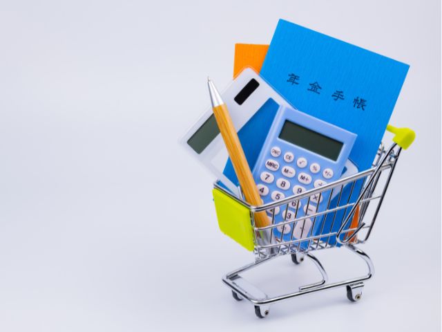 小さなショッピングカートに乗った年金手帳・電卓・鉛筆