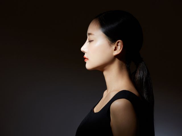 黒い背景の前に横向きに立つ若い日本人女性