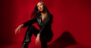 赤い背景の前でポーズをする黒いボディスーツの女性