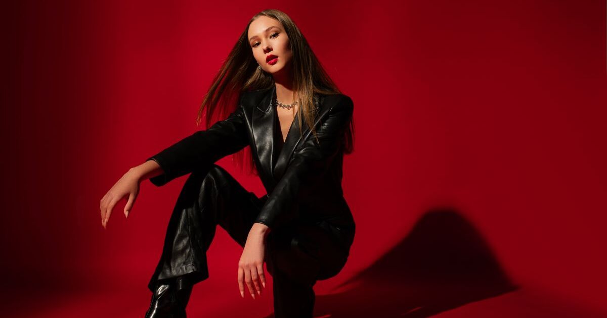 赤い背景の前でポーズをする黒いボディスーツの女性