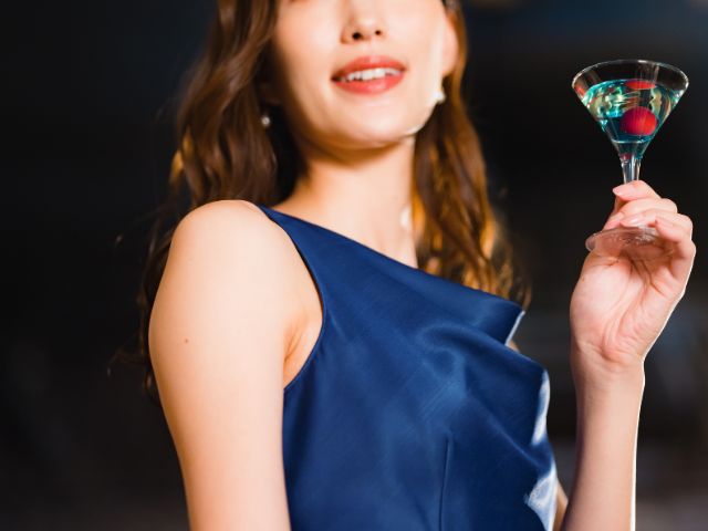 紺色のドレスを着て左手にお酒を持ったロングヘアの女性