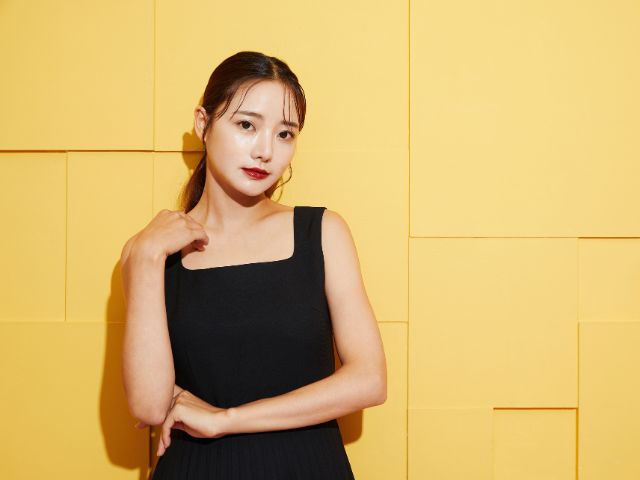 黄色い壁の前に立つ黒いドレスを着た若い日本人女性