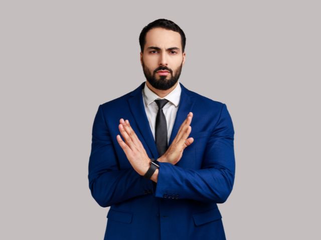 紺色のスーツを着て体の前でバツマークを作る外国人男性