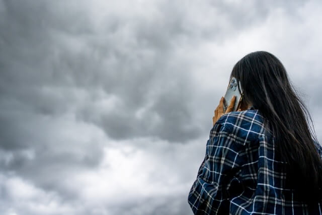 雲行きが怪しい空と電話をする女性