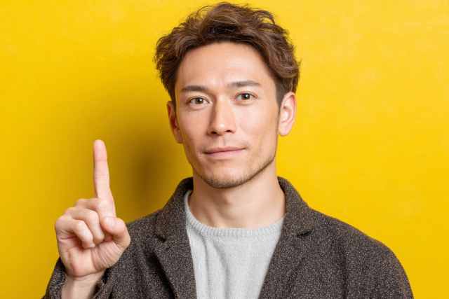 黄色い背景の前で人差し指を立てている男性