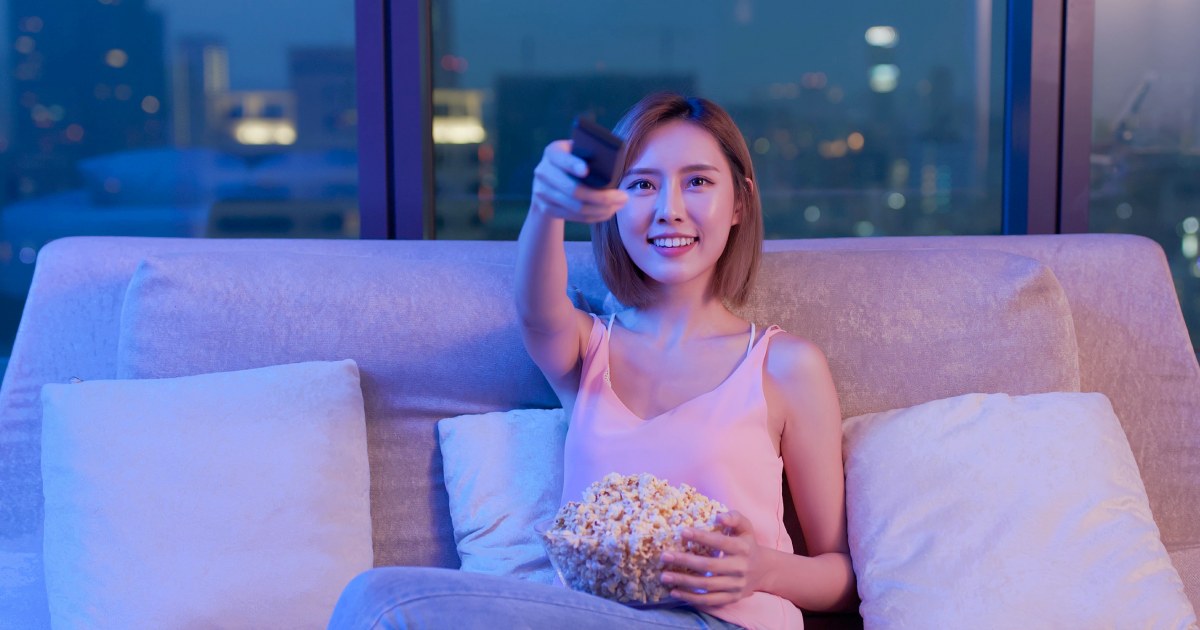 夜の自室でポップコーンを食べながら映画をみようとしている女性