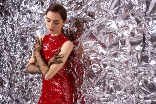 銀色の背景の前に立つ赤いドレスの女性