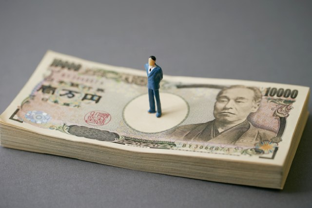 積み上げられた複数の一万円札の上に立つ男性のフィギュア