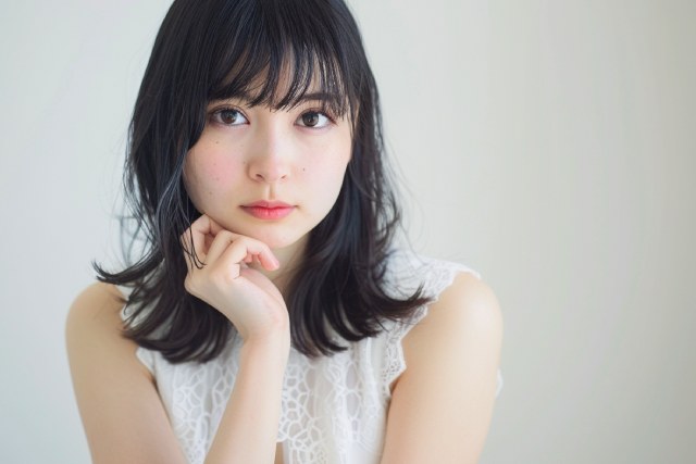 白いドレスを着て顎に手を当てている黒い髪の女性