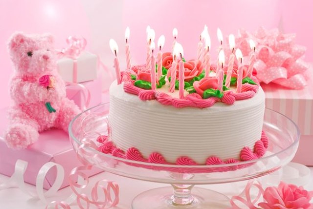ピンク色の背景に複数のろうそくが灯る誕生日ケーキ