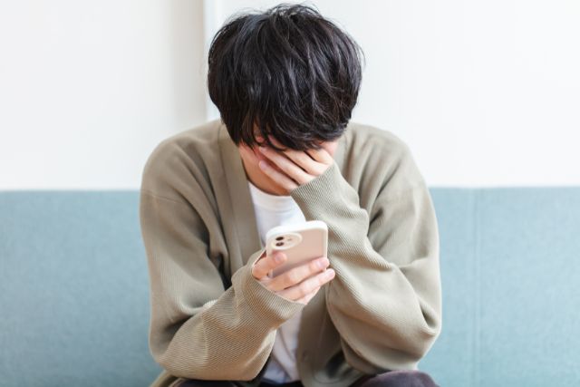 携帯を片手にソファにうつむいて座る男性