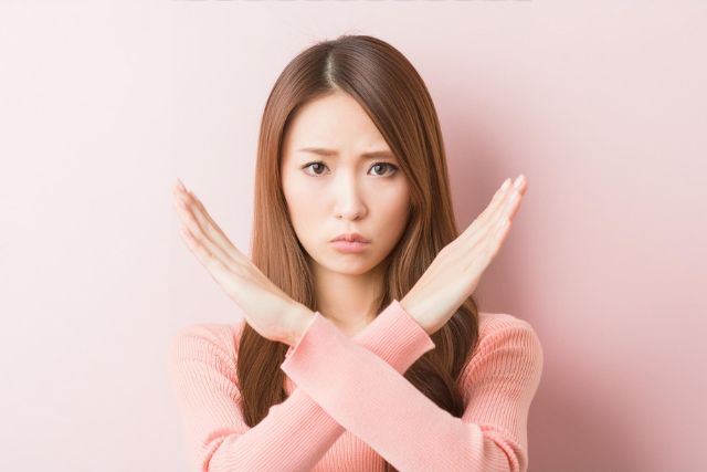 困った顔でておクロスさせバツのハンドサインをする女性