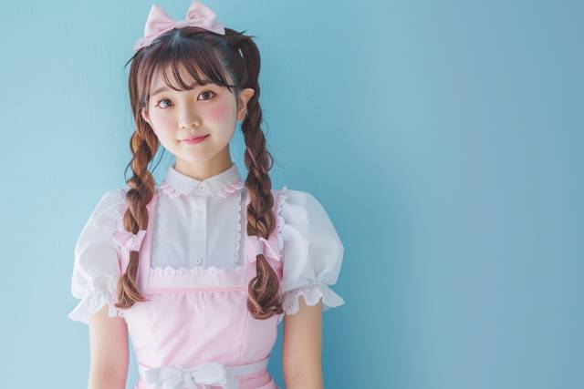 水色の背景の前でこちらを見るメイド服を着た女性